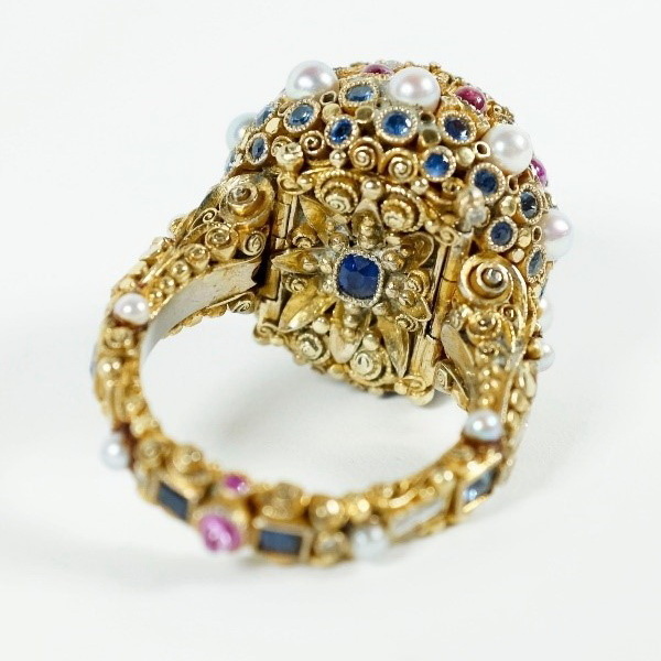 The rim of the ring is decorated with precious stones on the outer and inner sides; under the central stone there is a compartment with a hinged lid decorated with sapphire.