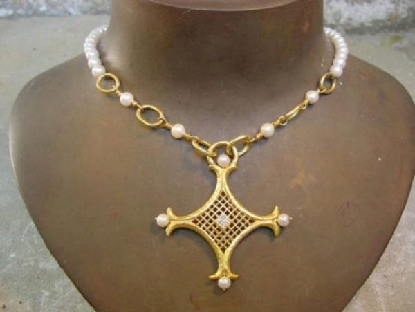 The Ravenna wedding necklace is a golden cross with a diamond enclosed in a cage at its core.